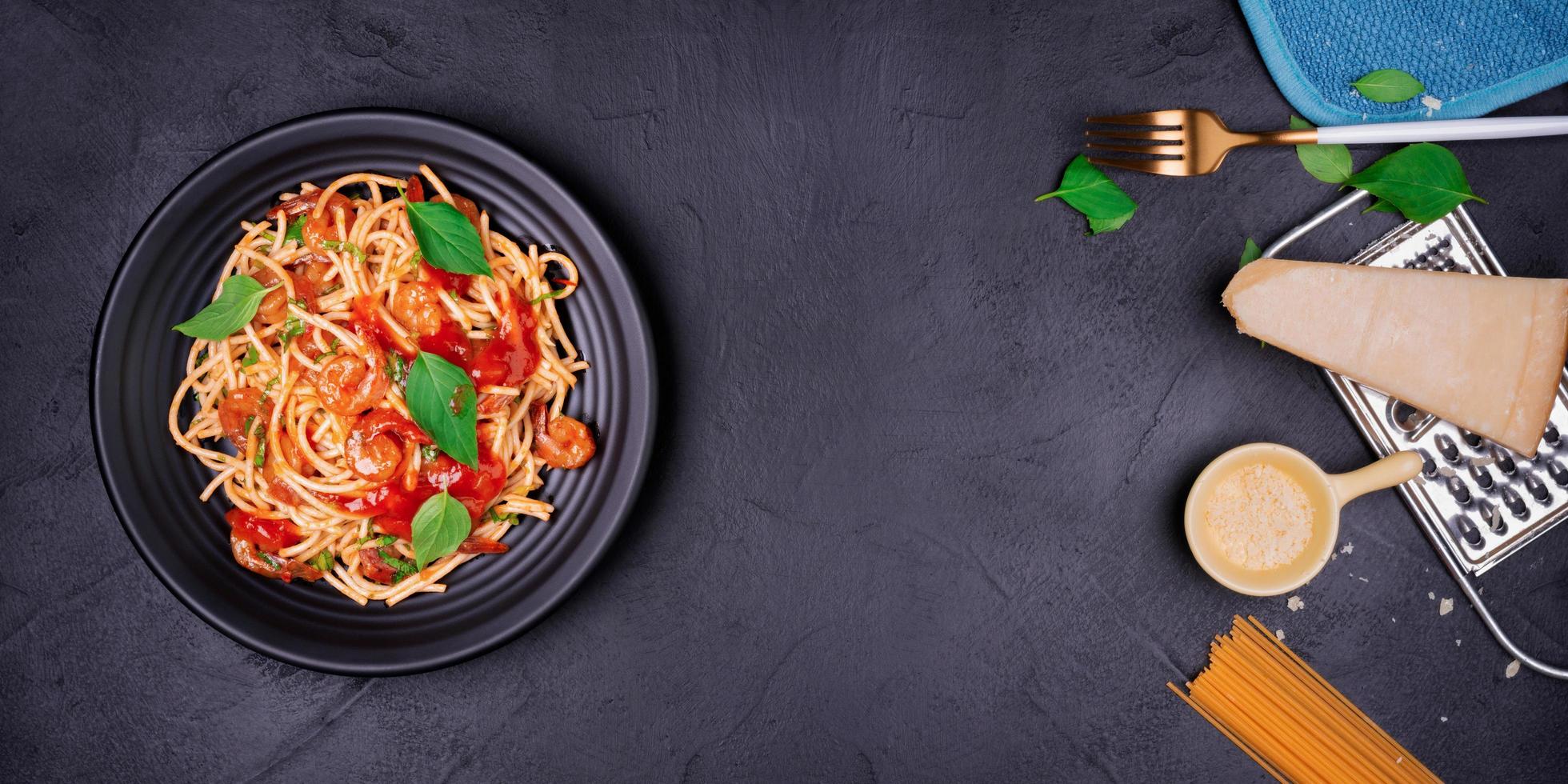 Delicious spaghetti pasta with prawns and cheese served on a black plate on a black background table Italian recipe, tomato sauce, vegetables, and spices top view with copy space photo