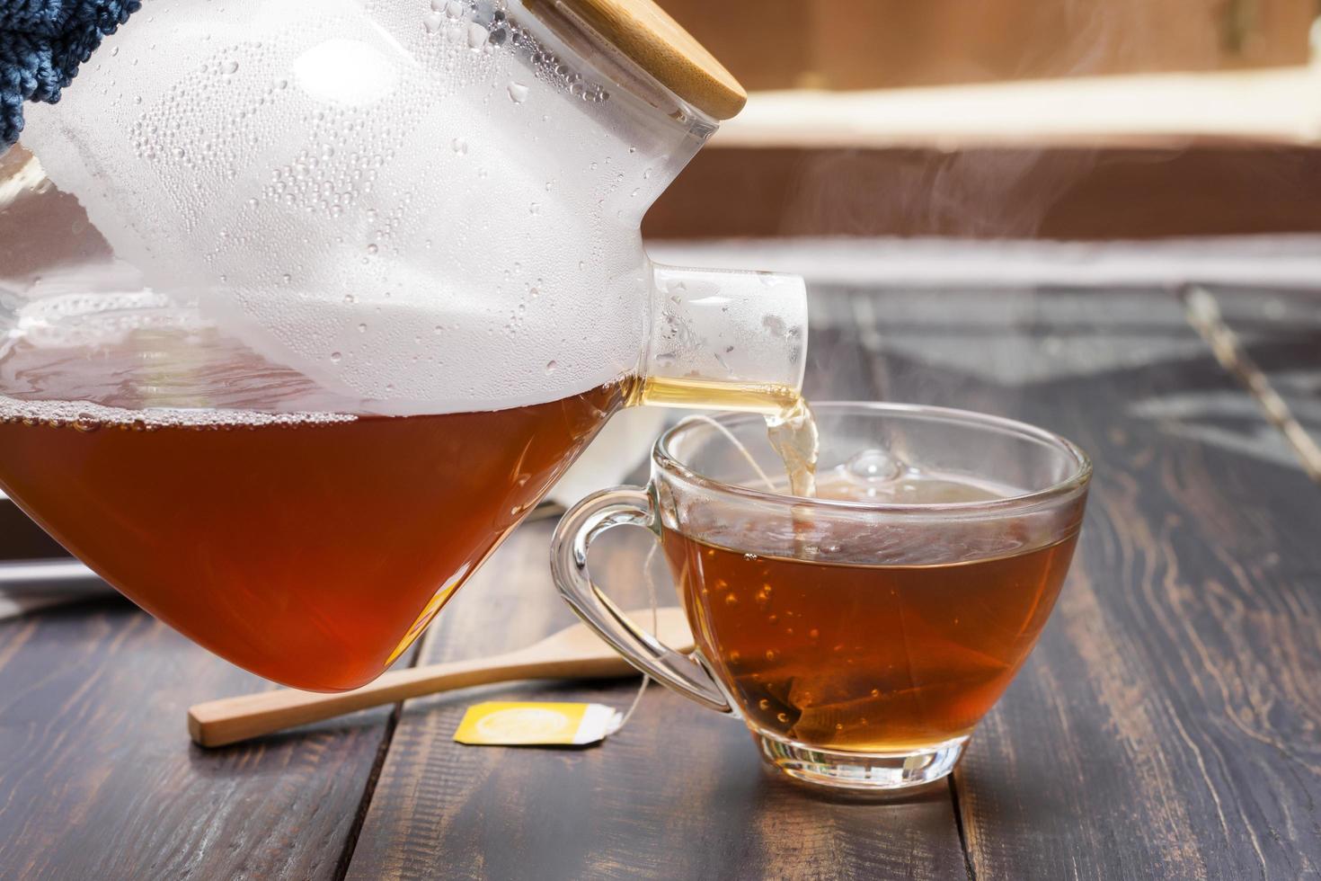 toma de primer plano de té o café caliente vertido en una taza colocada sobre el escritorio. o una mesa para sentarse a tomar café en el trabajo o en casa cerca de la ventana al atardecer o por la mañana foto