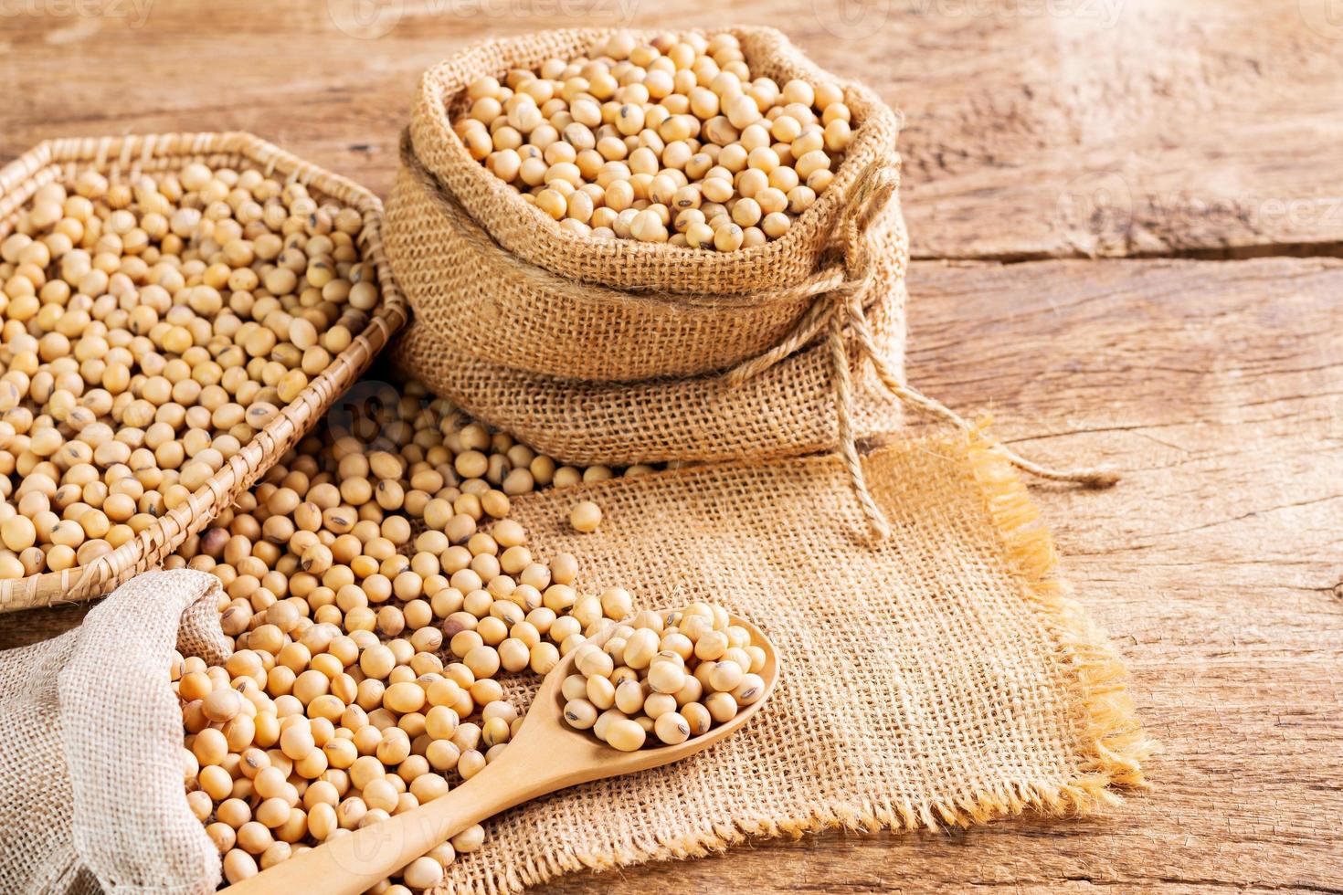 semillas de soja en una cuchara de madera y en un saco colocado sobre una mesa de madera semillas o alimentos saludables naturales - vista superior foto