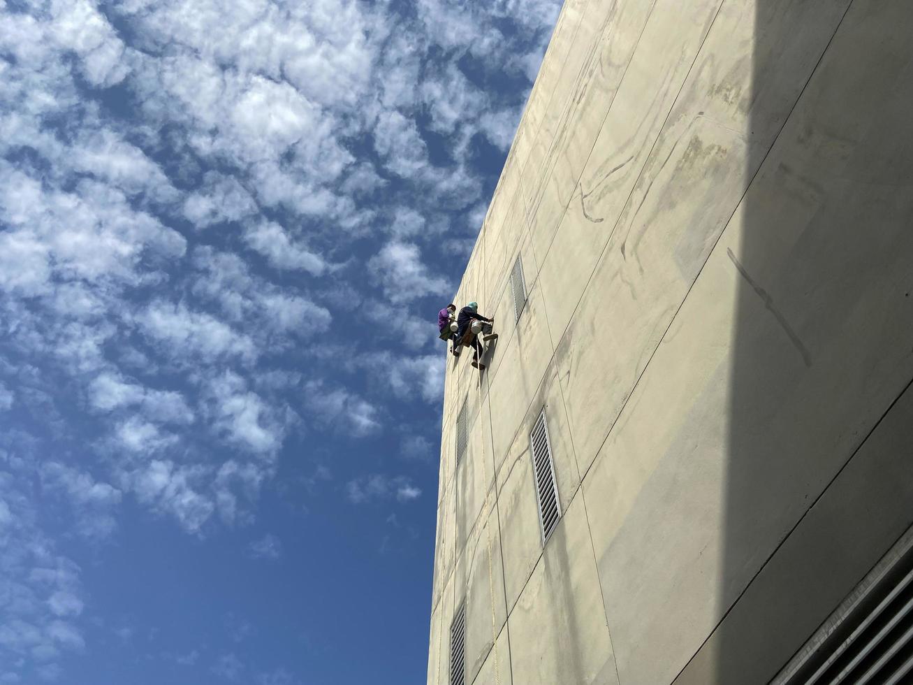 pintor arreglando la pared y pintando en la pared del trabajador de la construcción con un cepillo de rodillos trabaja en edificios altos sin equipo de seguridad el concepto de trabajo peligroso en alturas foto