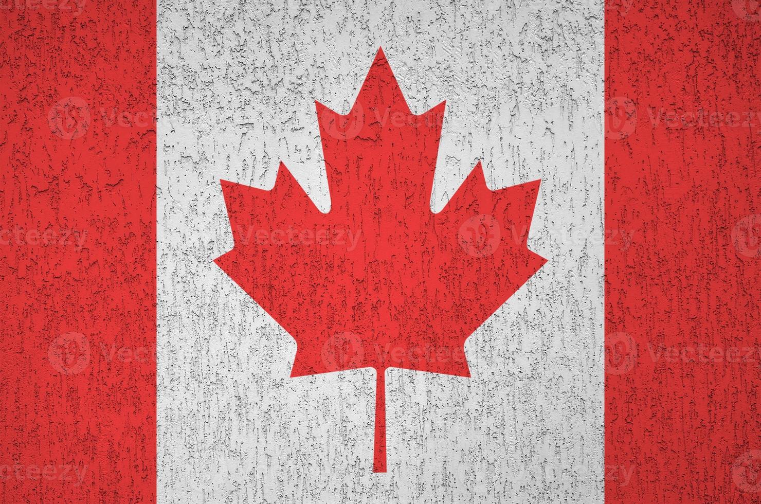 Canada flag depicted in bright paint colors on old relief plastering wall. Textured banner on rough background photo