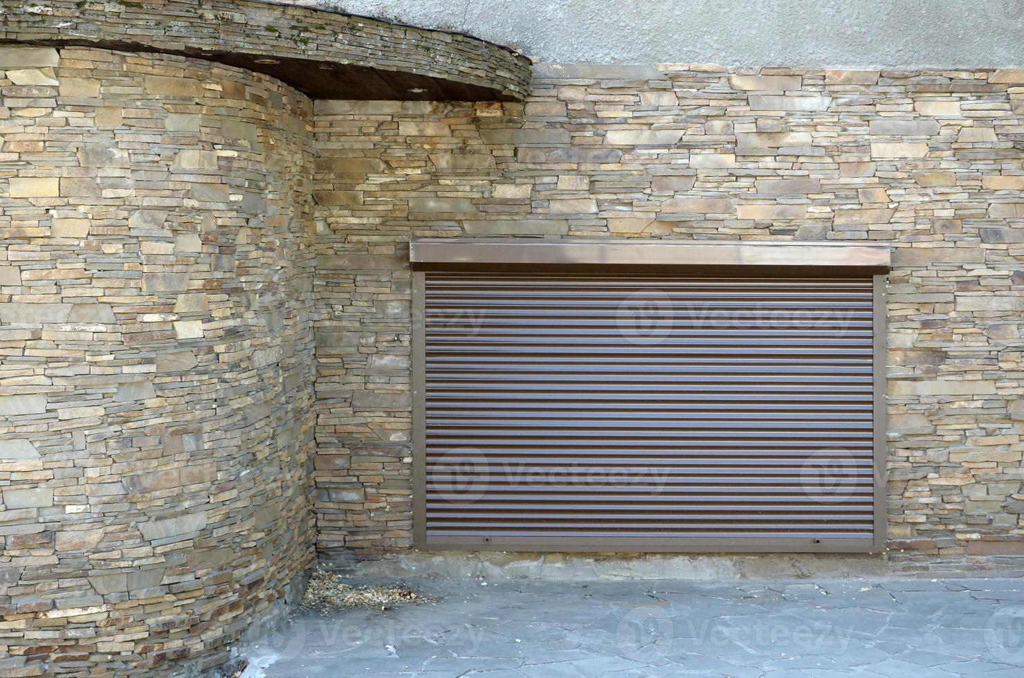 A window with brown metal rolling shutters and wall decoration with artificial stone photo