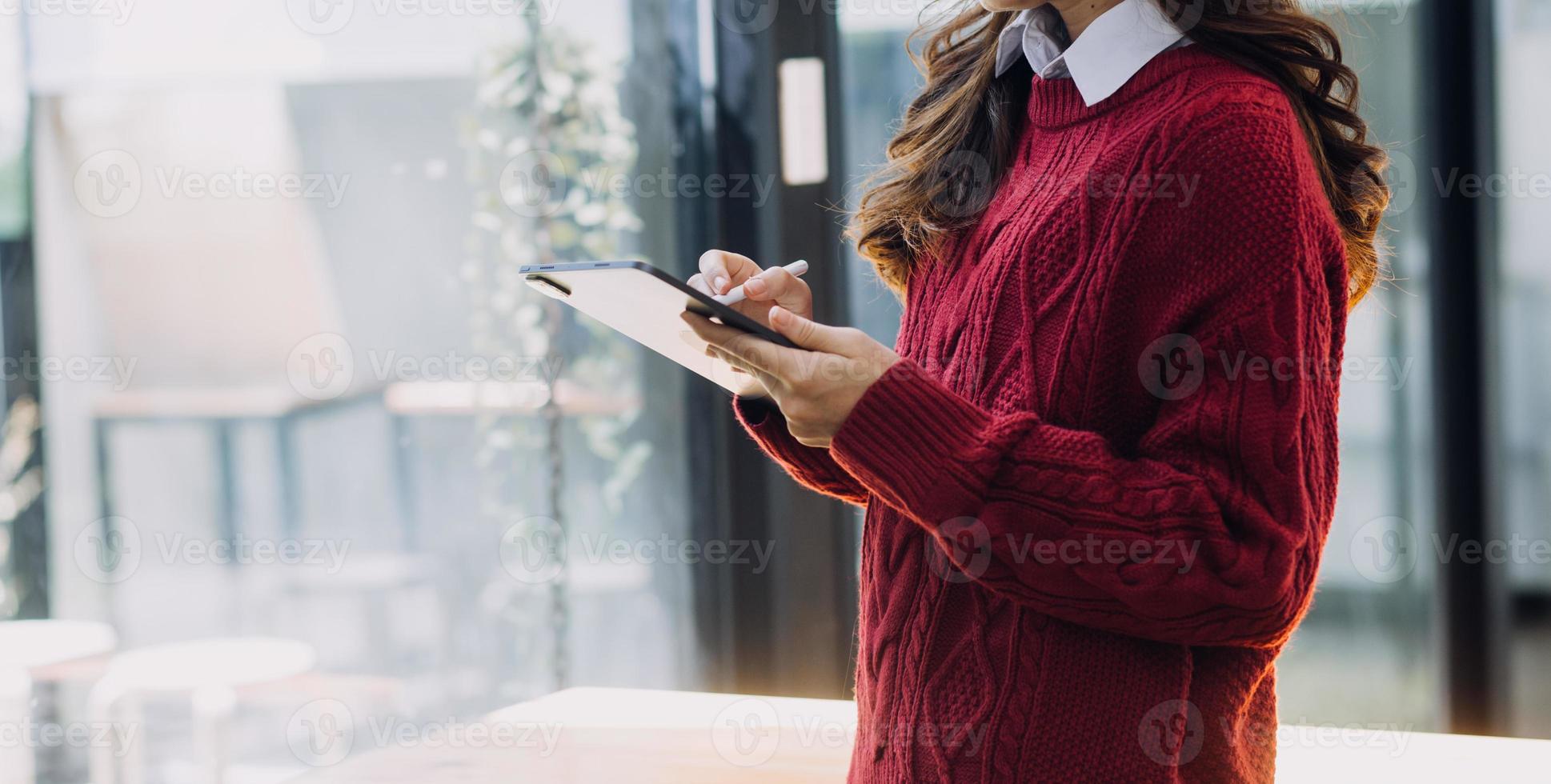 Young business woman sitting in office at table and using smartphone. On desk is laptop and tablet computer, on screen charts and graphs. Woman analyzing data. Student learning online. photo