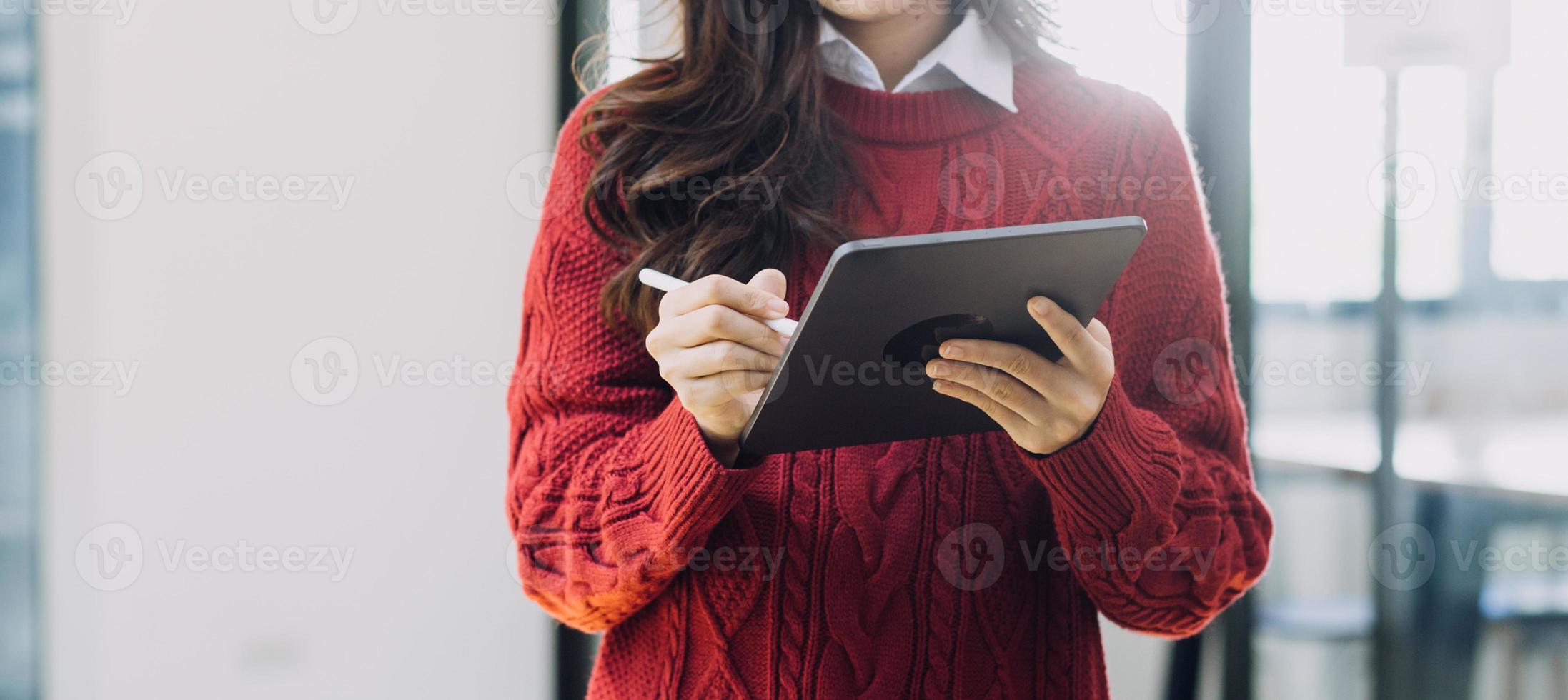 Young business woman sitting in office at table and using smartphone. On desk is laptop and tablet computer, on screen charts and graphs. Woman analyzing data. Student learning online. photo
