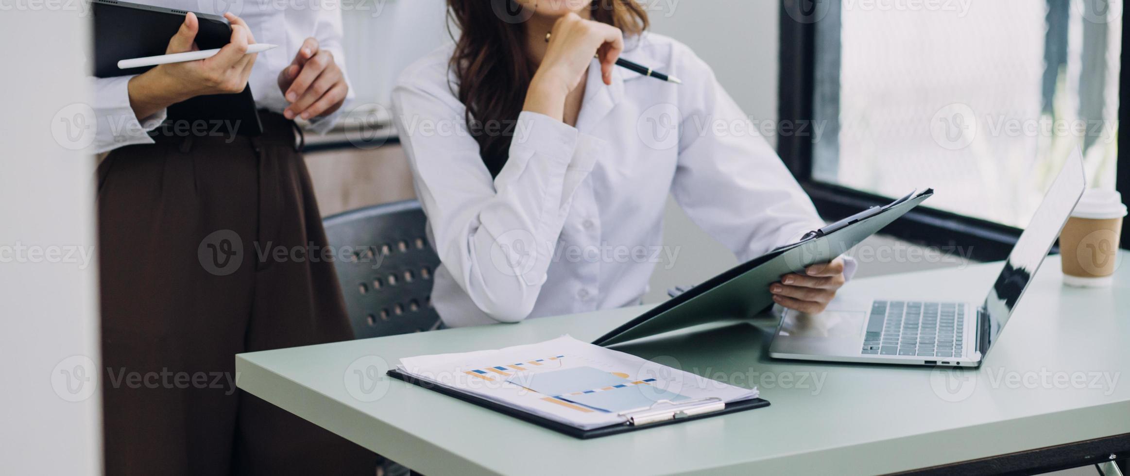 Young business woman sitting in office at table and using smartphone. On desk is laptop and tablet computer, on screen charts and graphs. Woman analyzing data. Student learning online. photo
