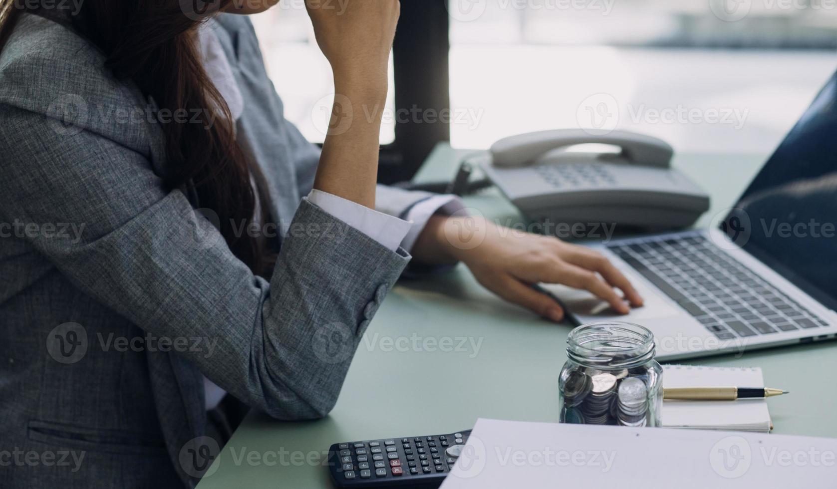 Young business woman sitting in office at table and using smartphone. On desk is laptop and tablet computer, on screen charts and graphs. Woman analyzing data. Student learning online. photo