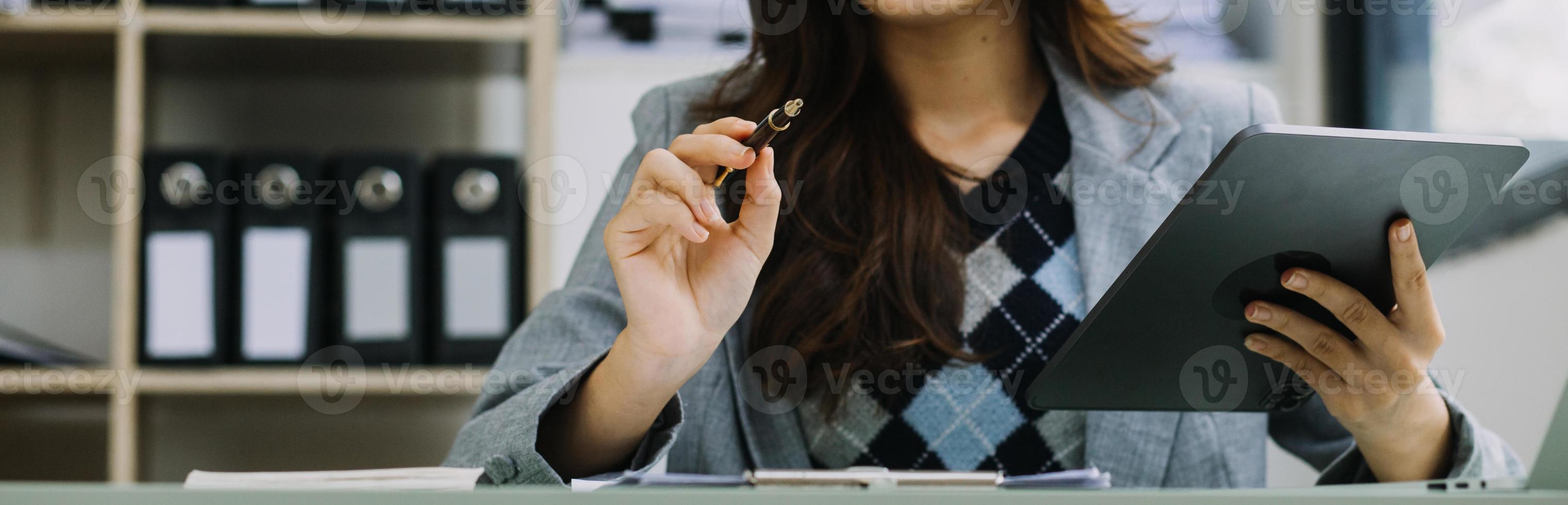 Young business woman sitting in office at table and using smartphone. On desk is laptop and tablet computer, on screen charts and graphs. Woman analyzing data. Student learning online. photo