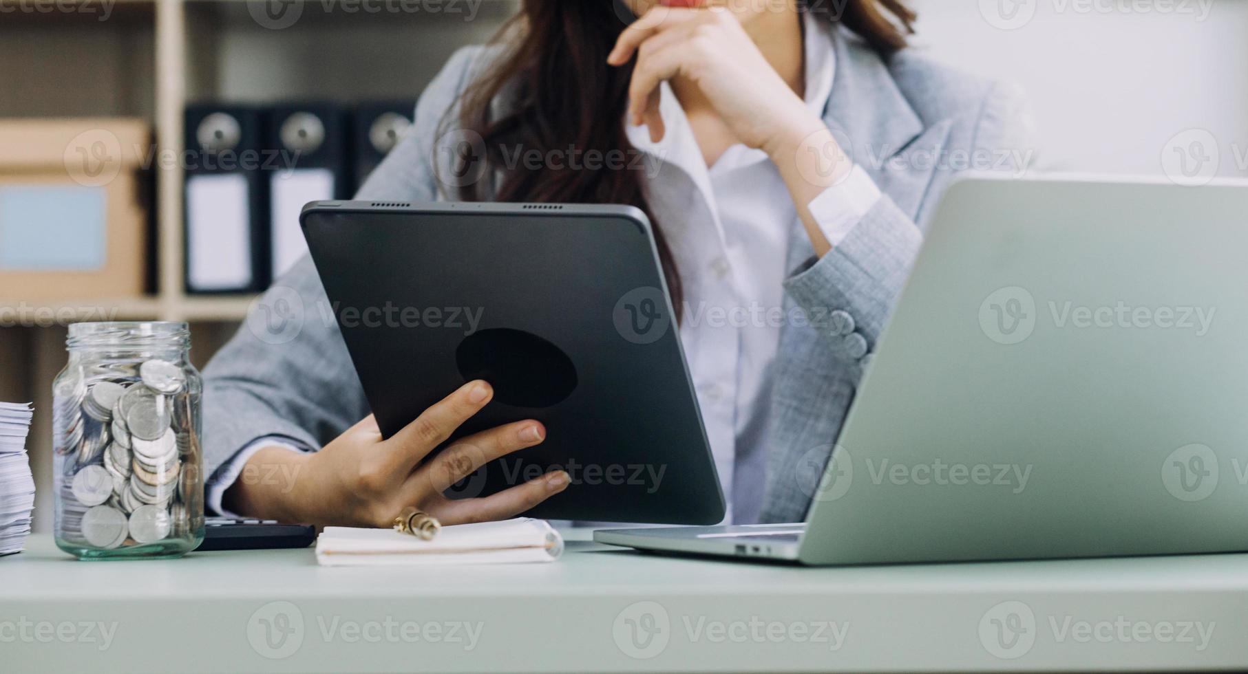 Young business woman sitting in office at table and using smartphone. On desk is laptop and tablet computer, on screen charts and graphs. Woman analyzing data. Student learning online. photo