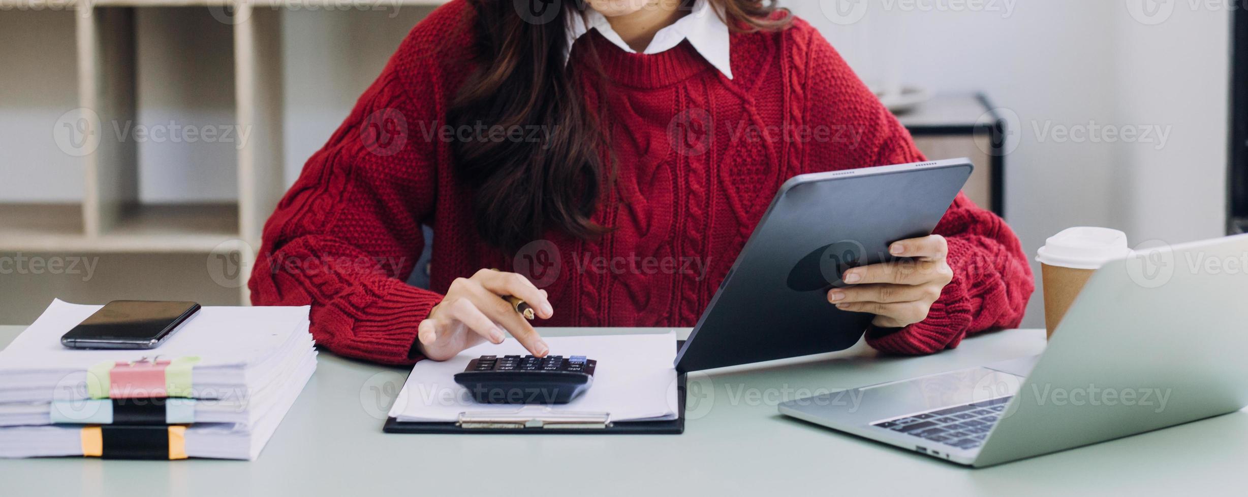 Young business woman sitting in office at table and using smartphone. On desk is laptop and tablet computer, on screen charts and graphs. Woman analyzing data. Student learning online. photo