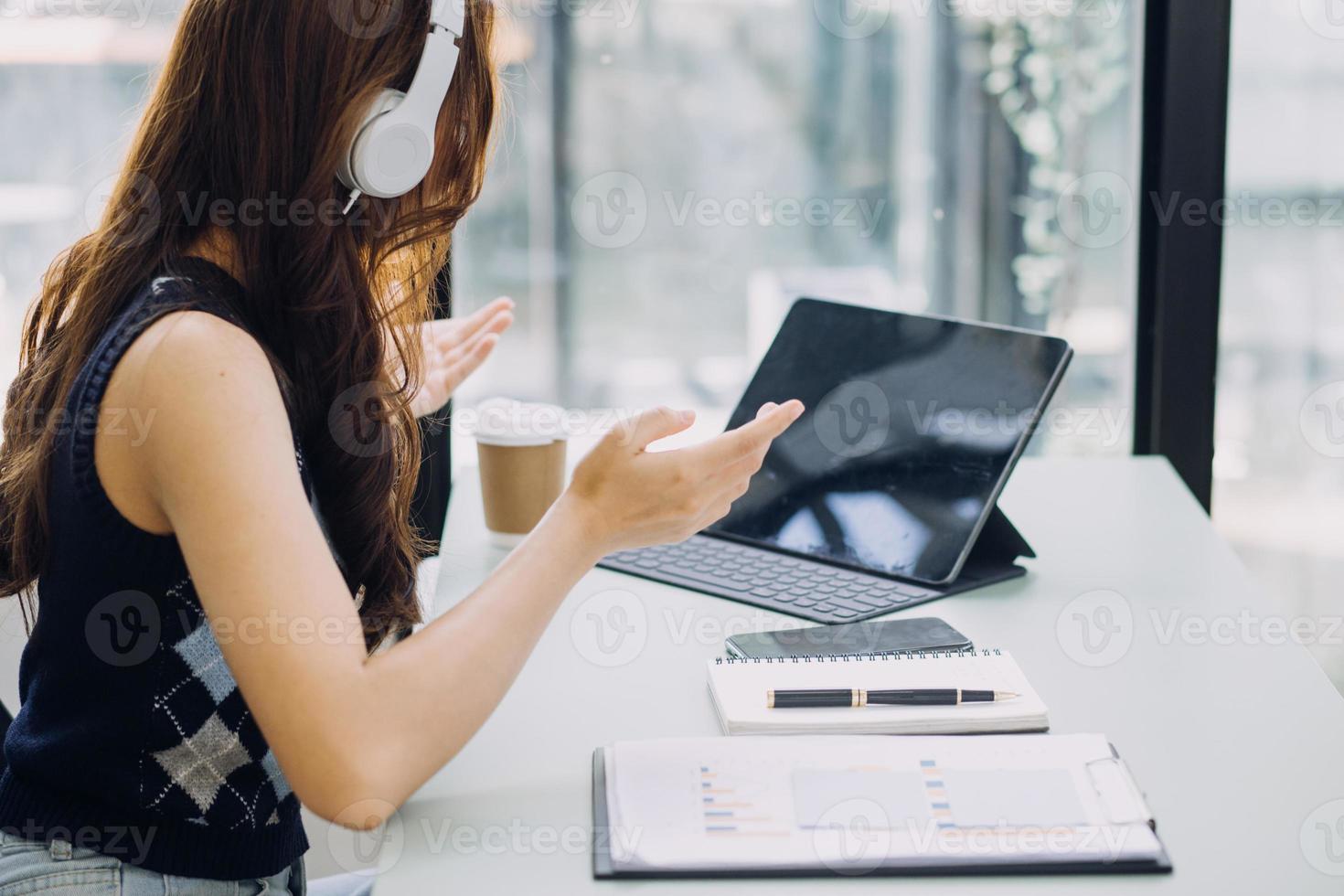 Young business woman sitting in office at table and using smartphone. On desk is laptop and tablet computer, on screen charts and graphs. Woman analyzing data. Student learning online. photo