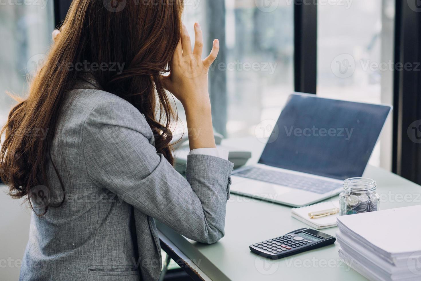 Young business woman sitting in office at table and using smartphone. On desk is laptop and tablet computer, on screen charts and graphs. Woman analyzing data. Student learning online. photo