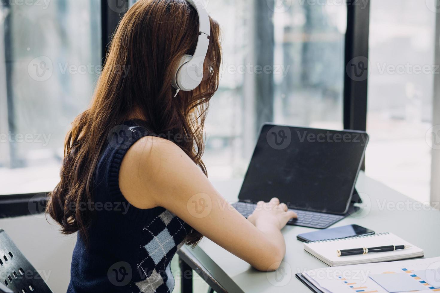 Young business woman sitting in office at table and using smartphone. On desk is laptop and tablet computer, on screen charts and graphs. Woman analyzing data. Student learning online. photo