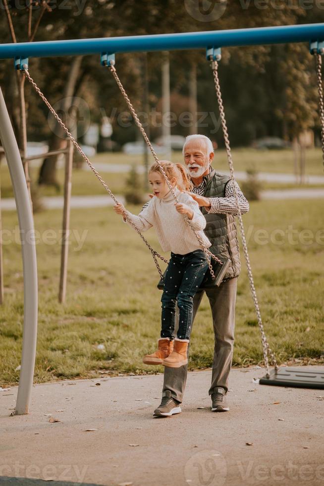 Grandfather spending time with his granddaughter in park playground on autumn day photo