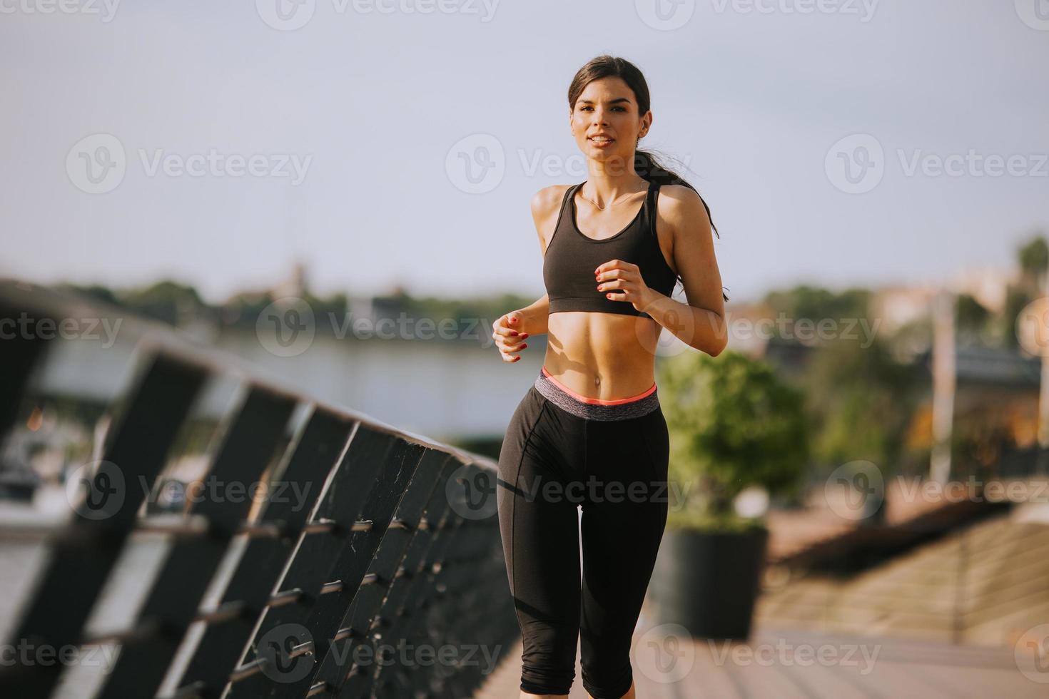 hermosa mujer joven activa corriendo en el paseo marítimo a lo largo de la orilla del río foto