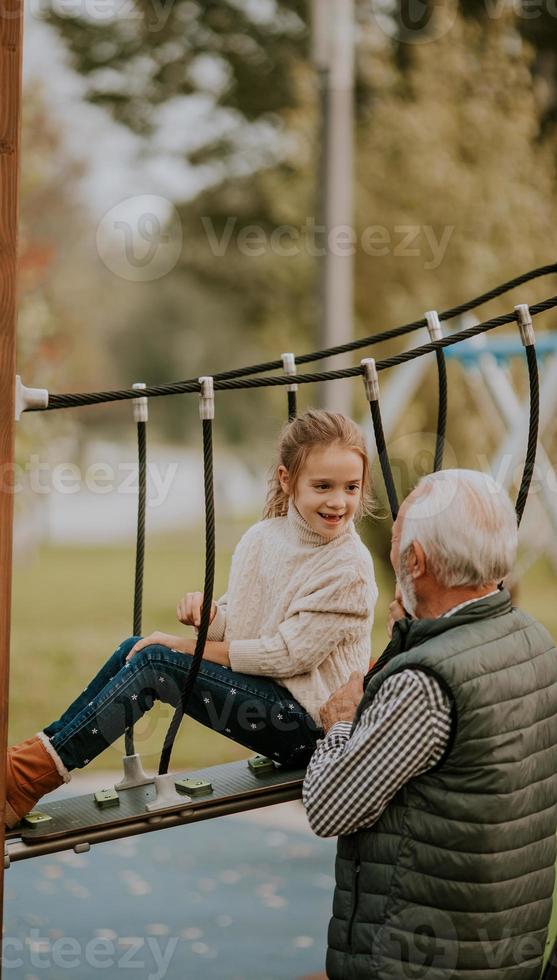 el abuelo pasa tiempo con su nieta en el parque infantil el día de otoño foto