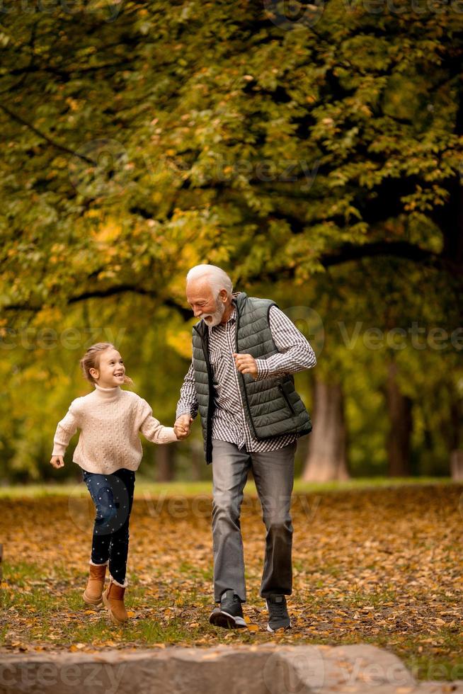 Grandfather spending time with his granddaughter in park on autumn day photo