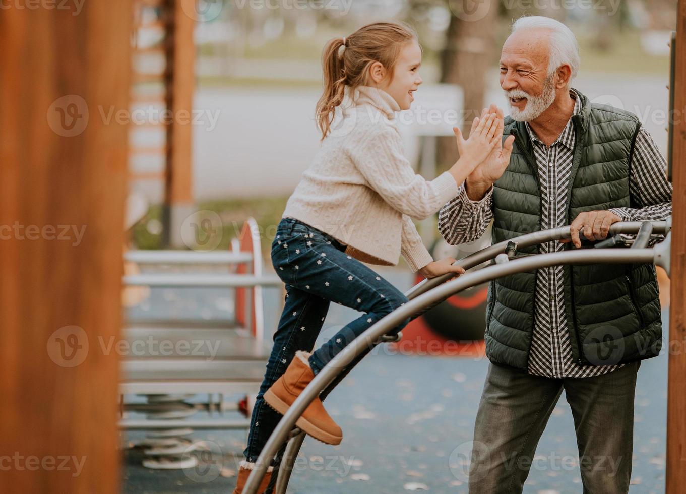 Grandfather spending time with his granddaughter in park playground on autumn day photo