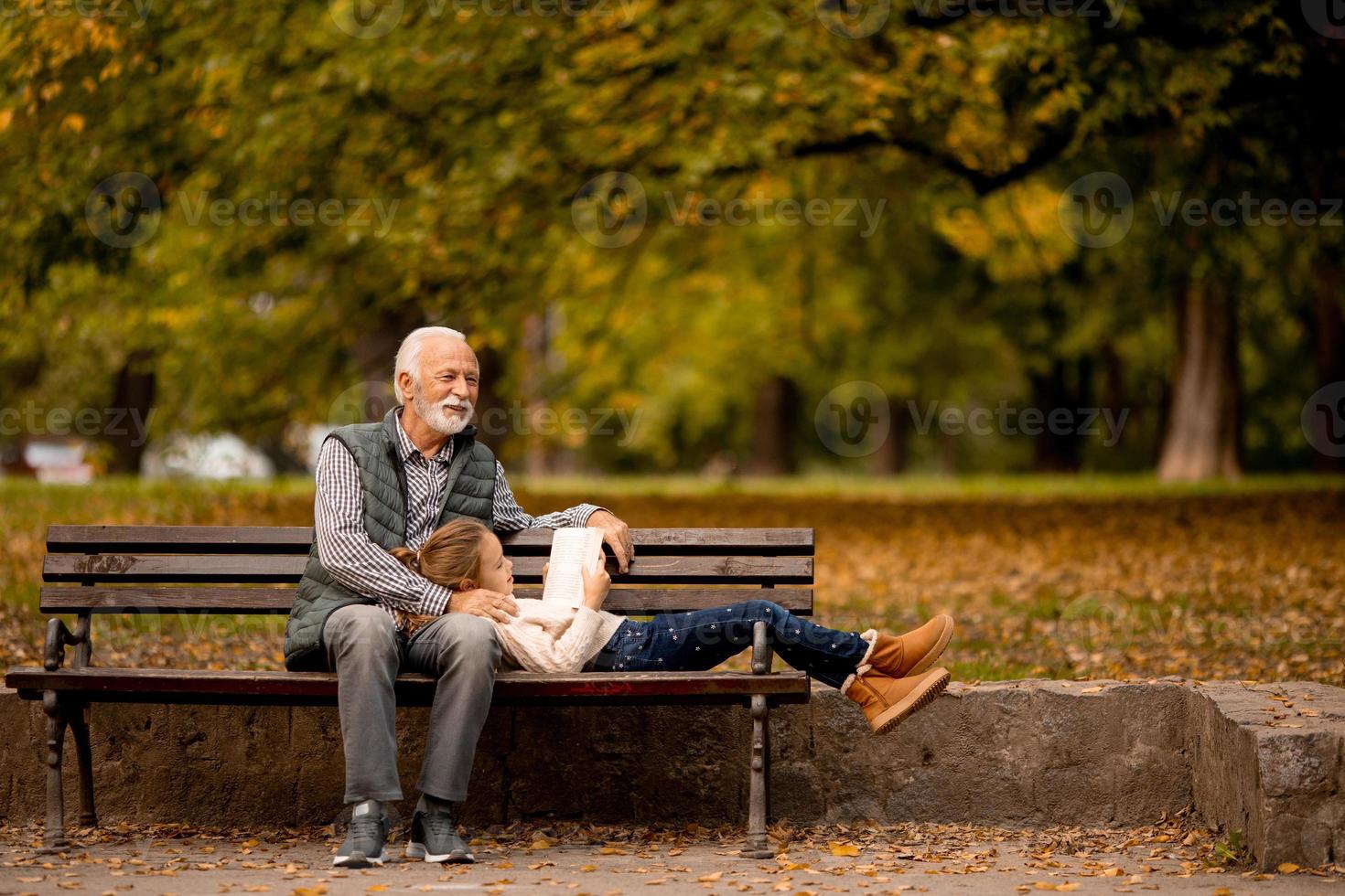 Grandfather spending time with his granddaughter on bench in park on autumn day photo