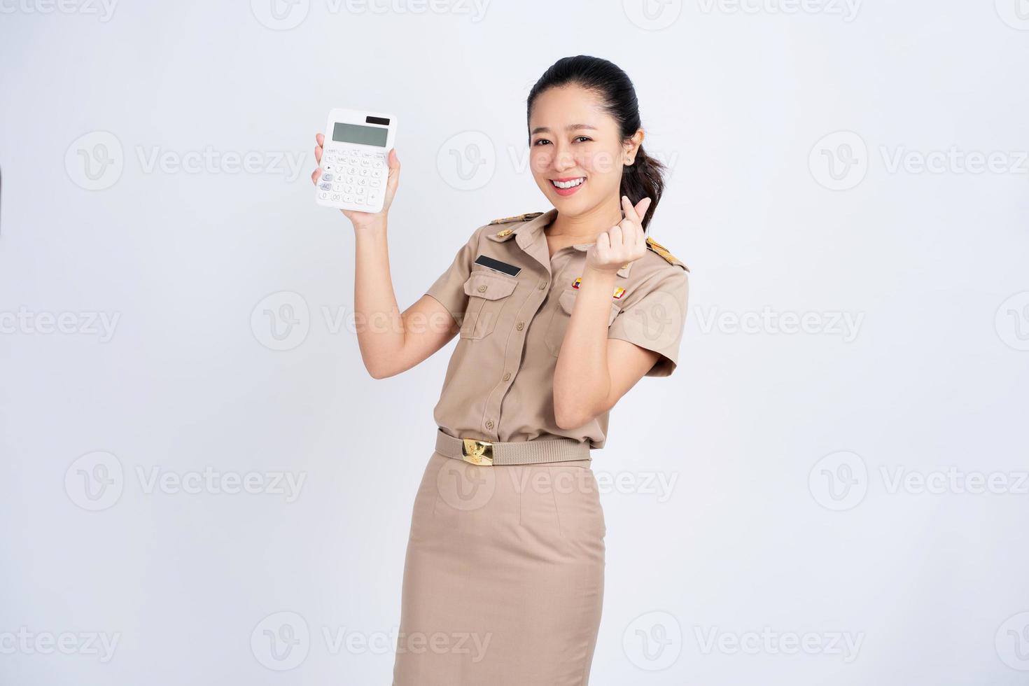 Portrait of excited Asian woman in brown uniform work clothes she holding calculator isolated on white background, Business and financial concept photo
