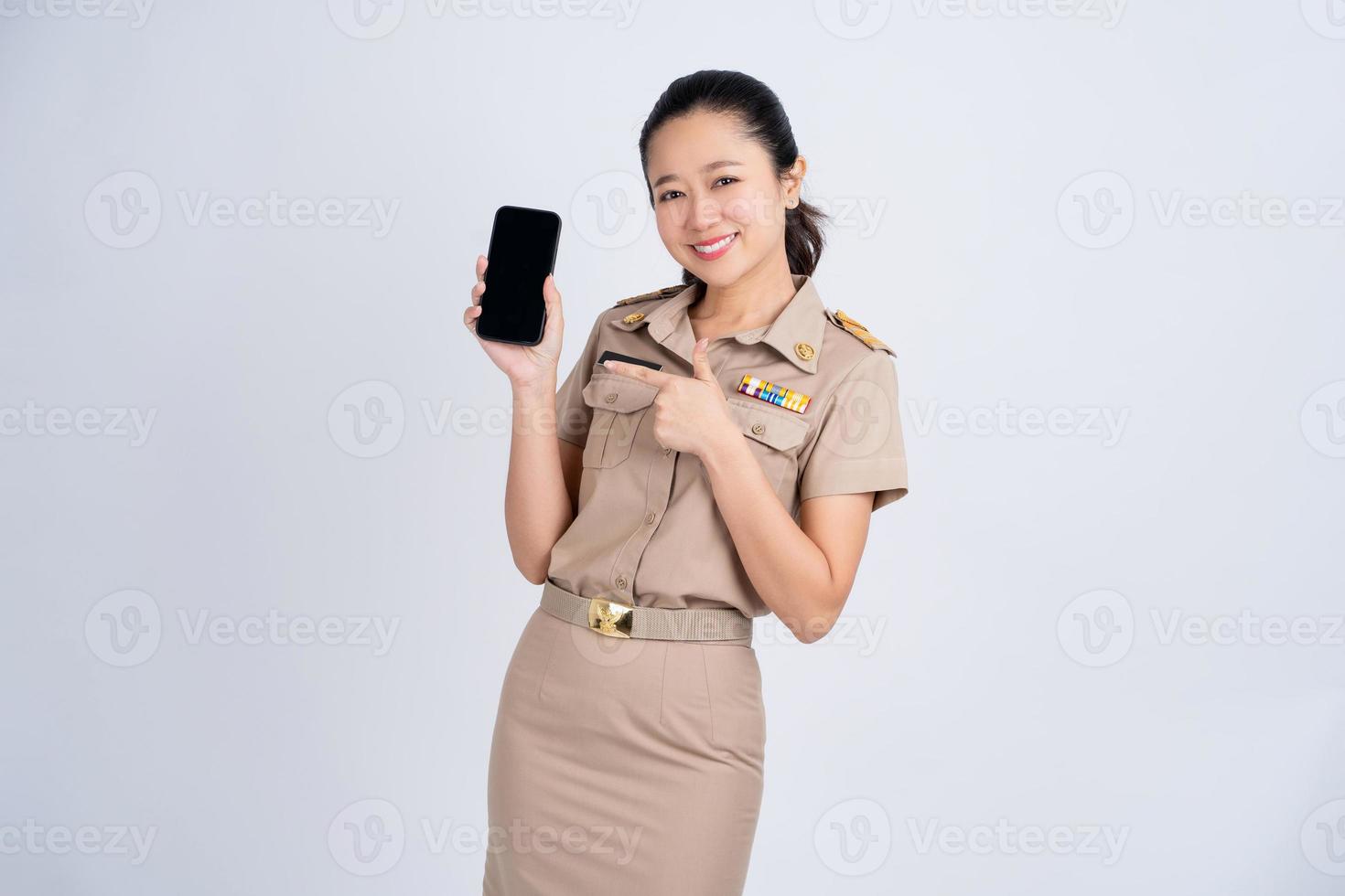 retrato de mujer asiática en ropa de trabajo marrón. ella muestra o presenta una aplicación de teléfono móvil aislada sobre fondo blanco, modelo asiático tailandés foto