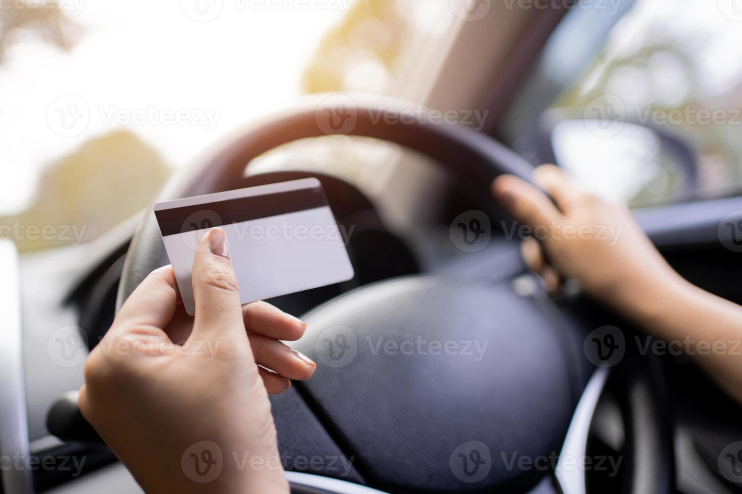 A woman holding a credit card, she's in the car, she stops filling up the gas station and paying with credit card. Credit card concept. photo