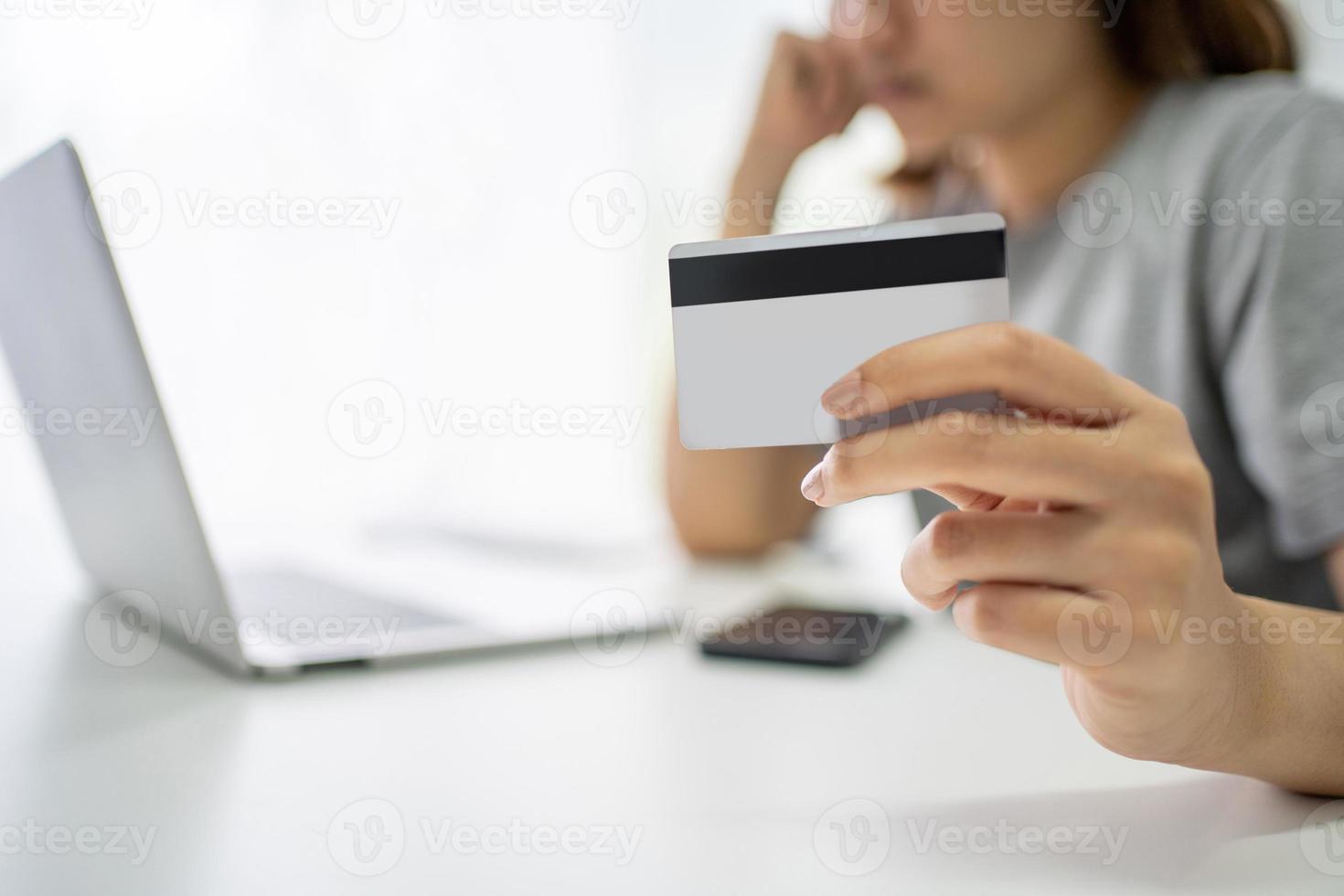 Stressed young woman with tax and debt problems from online shopping. She is holding a credit card on the table. Close up. photo