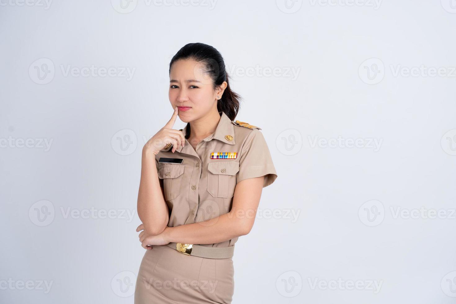 retrato asiático hermosa mujer joven en ropa de trabajo marrón. ella, sonriente, de pie con las manos en la barbilla, relajada pensando en algo sobre la pregunta. foto