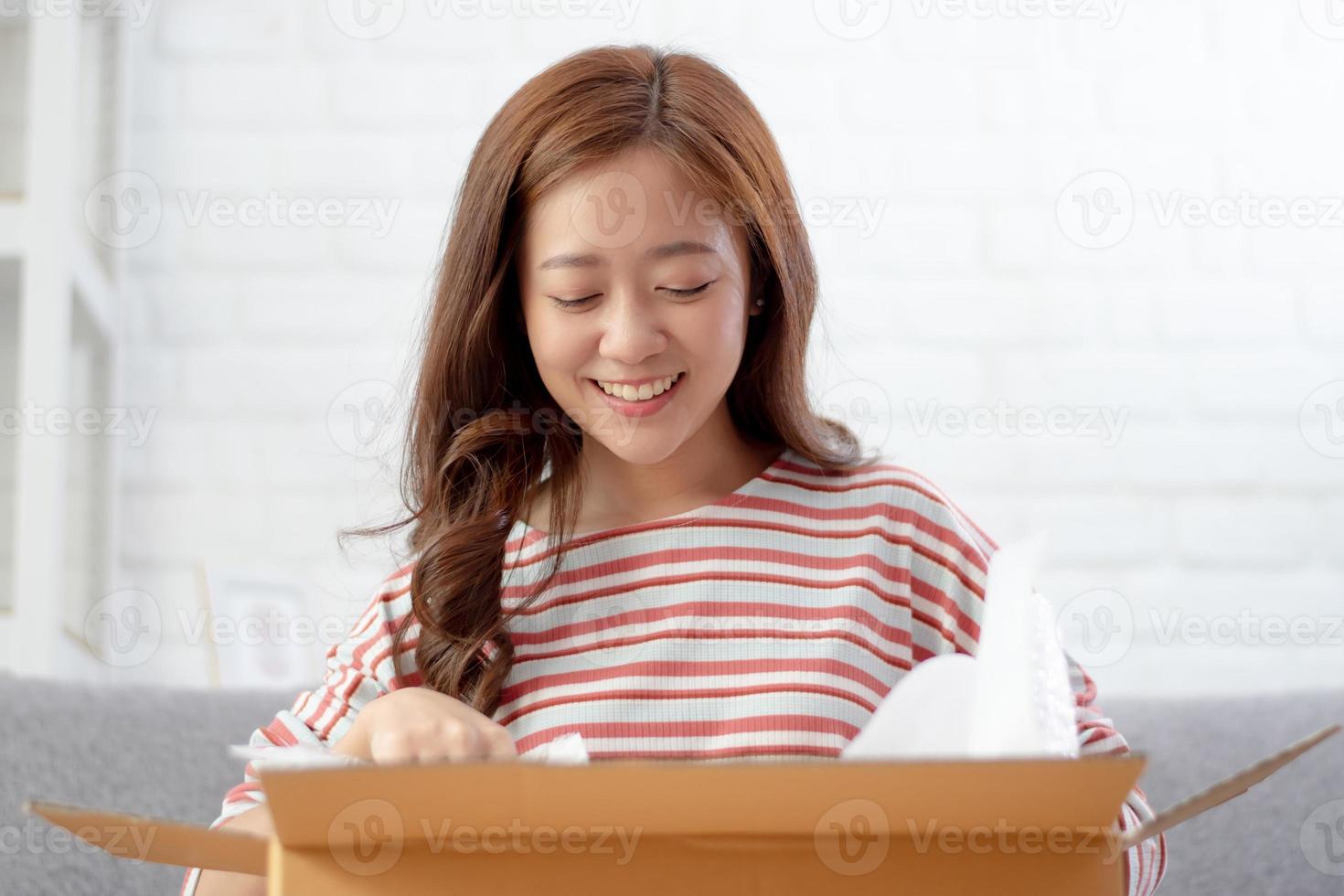 una mujer asiática feliz y sonriente está sacando cosas de una caja ordenada por Internet. concepto de compras en línea foto