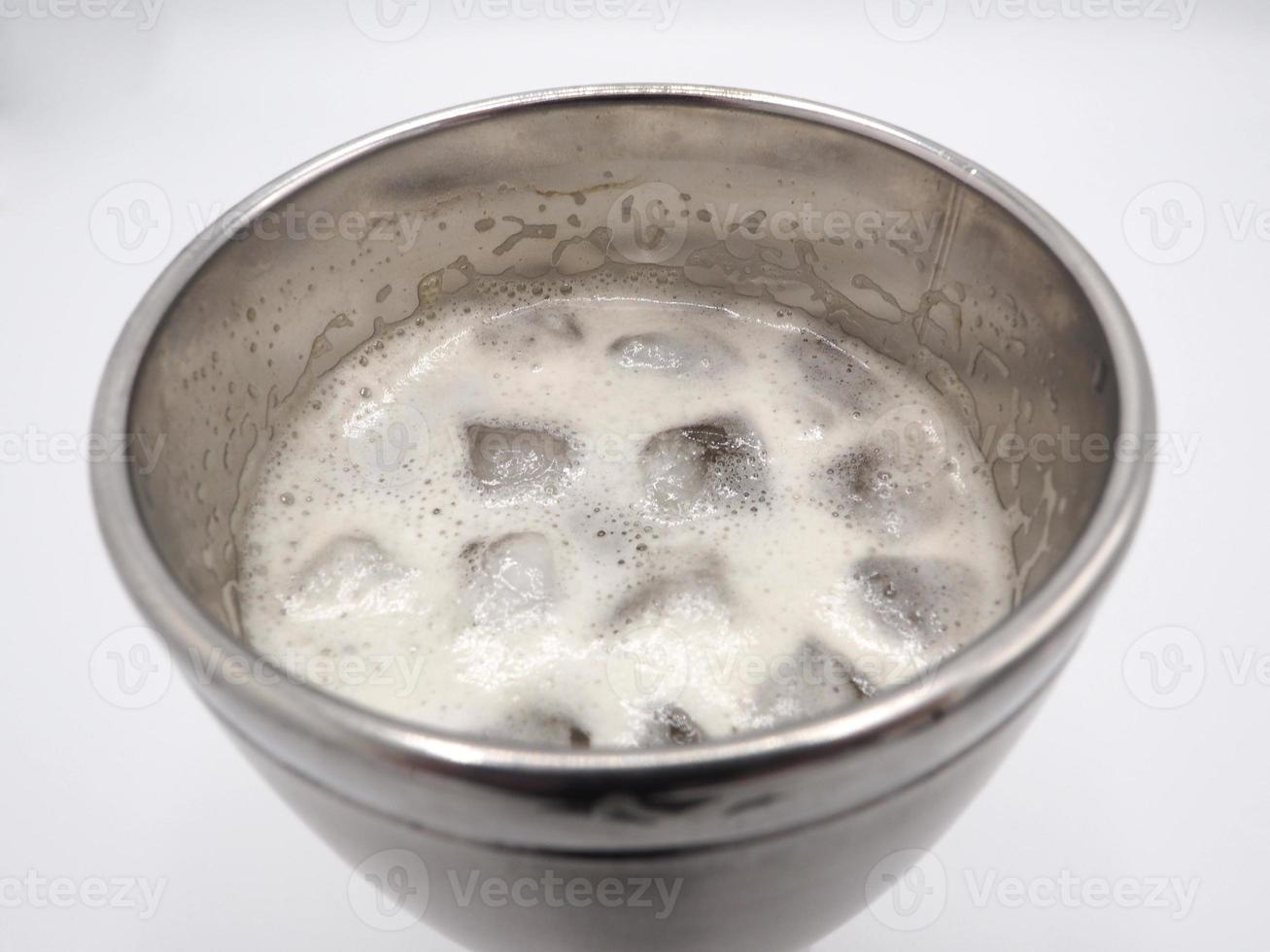 White beer foam bubbles and ice cubes close-up in the stainless steel thermos mug top view and white background. photo