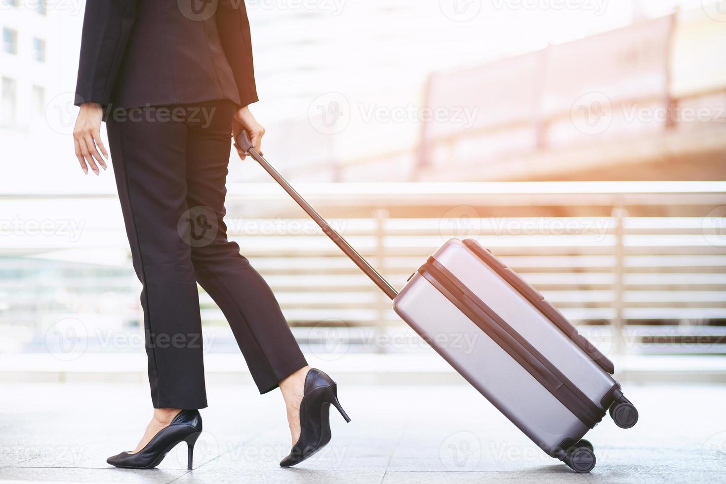 business woman walking outside public transport building with luggage in rush hour. Business traveler pulling suitcase in modern airport terminal. baggage business Trip. photo
