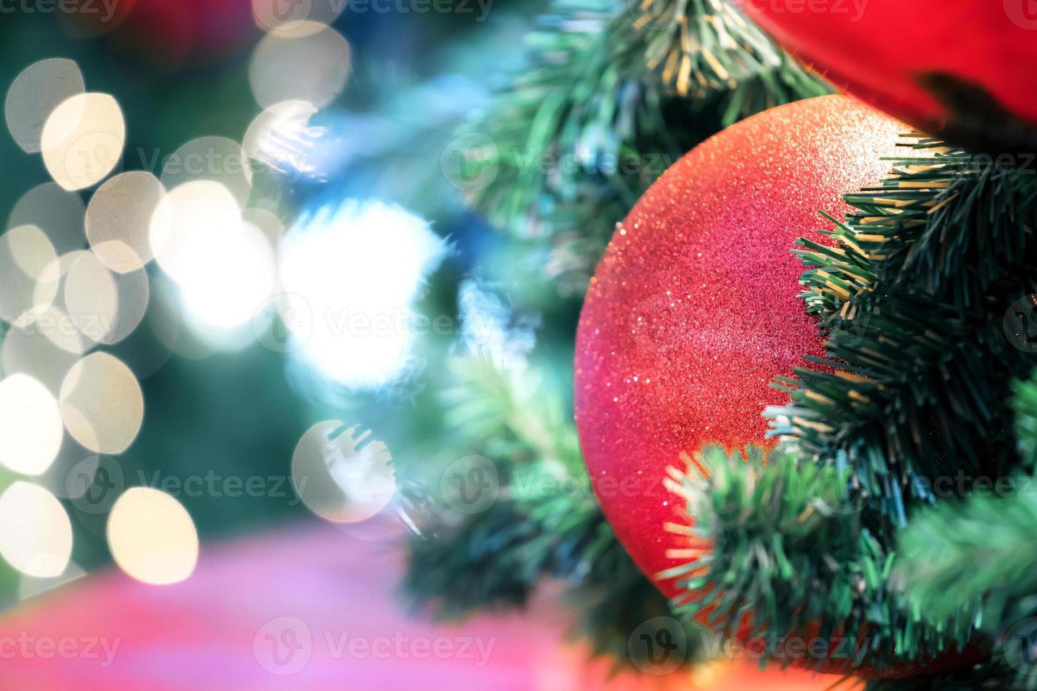 Closeup of red bauble hanging from a decorated christmas tree on blurred of  lights with decorated tree, sparkling and bokeh background. copy space for your text. photo