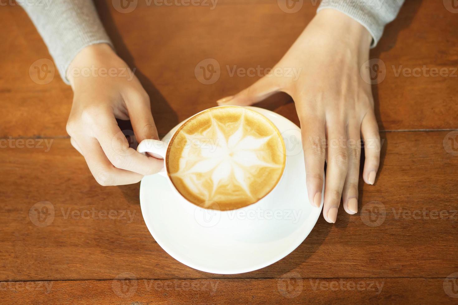 la gente sostiene una taza de café caliente con espuma en forma de árbol de flores lista para beber en una mesa de madera rústica, vista superior. estilo vintage de tono de filtro. foto