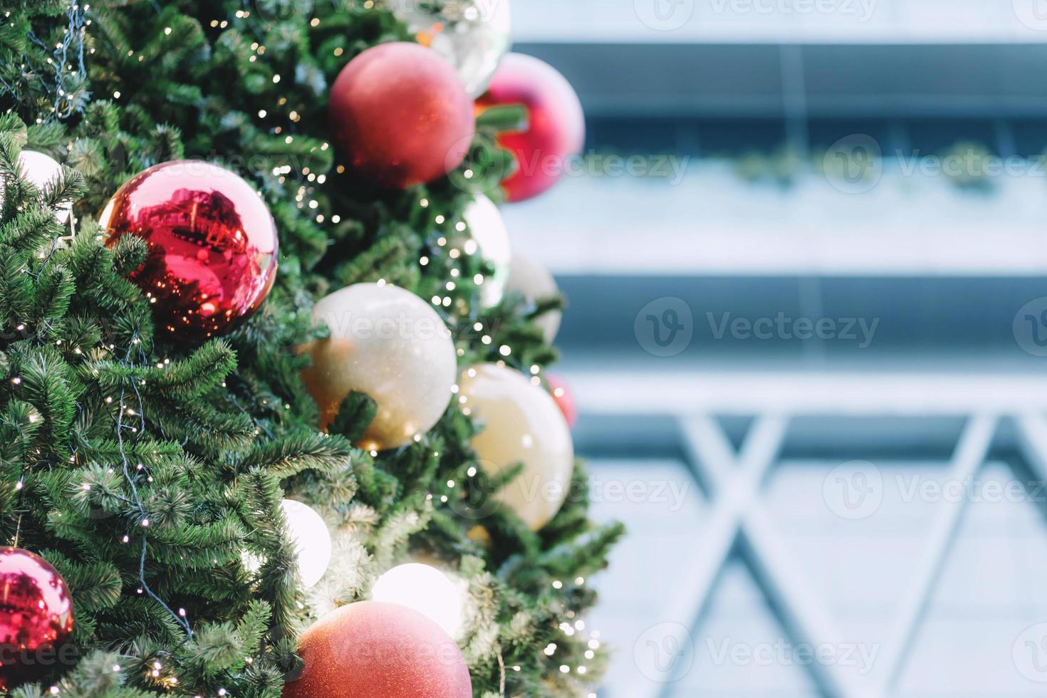 Closeup of red bauble hanging from a decorated christmas tree on blurred of  lights with decorated tree, sparkling and bokeh background. copy space for your text. photo