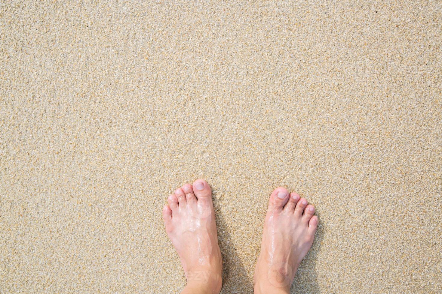 Cerca de los pies descalzos de un hombre parados mojados en la playa. foto