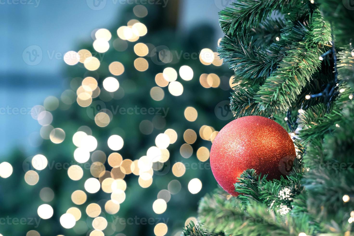 Closeup of red bauble hanging from a decorated christmas tree on blurred of  lights with decorated tree, sparkling and bokeh background. copy space for your text. photo
