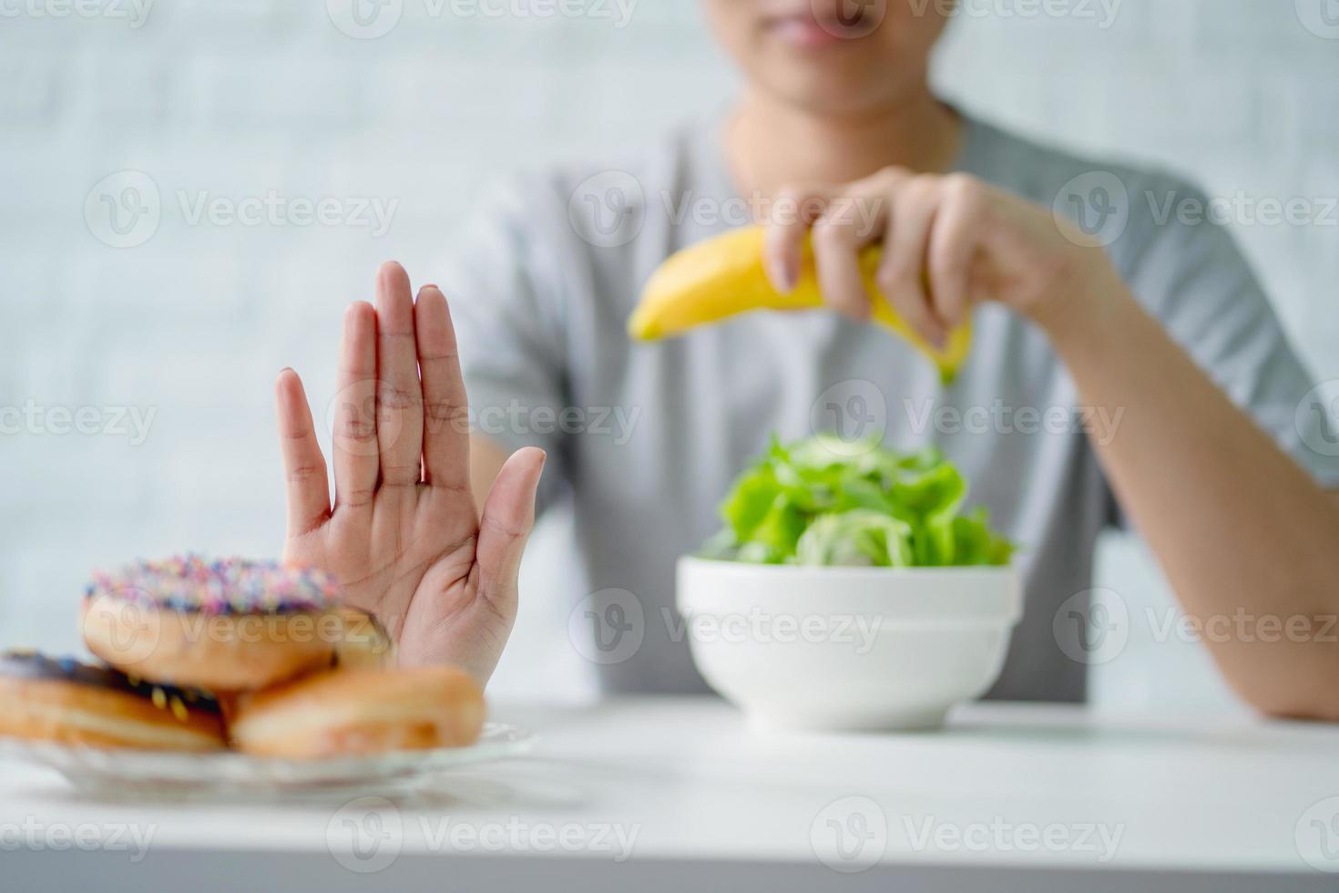 Young woman rejecting junk food or unhealthy food such as donut and choosing healthy food such as green apple and salad for her health. photo