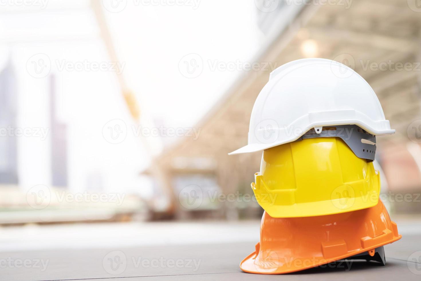 sombrero de casco de seguridad duro amarillo y blanco en el proyecto en el edificio del sitio de construcción en el piso de concreto en la ciudad con luz solar. casco para obrero como ingeniero o trabajador. concepto de seguridad primero. foto