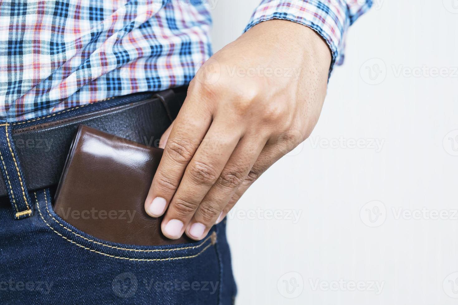 cierra a un hombre confiado posando en una caja fuerte guardando el dinero de tu billetera en el bolsillo delantero de sus pantalones vaqueros de bolsillo delantero. fondo papel pintado blanco foto