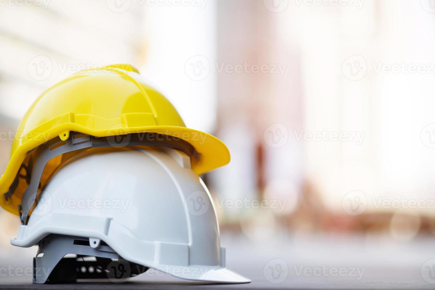 sombrero de casco de seguridad duro amarillo y blanco en el proyecto en el edificio del sitio de construcción en el piso de concreto en la ciudad con luz solar. casco para obrero como ingeniero o trabajador. concepto de seguridad primero. foto