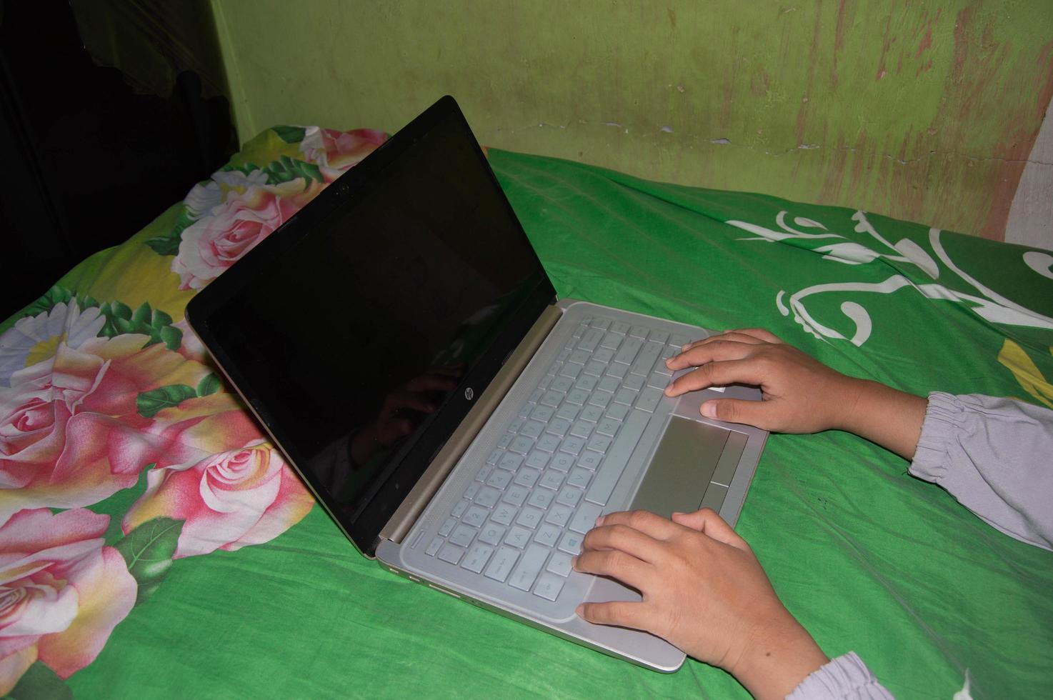 gresik, indonesia, 2022 - la mano de una mujer jugando en una computadora portátil. una mujer que trabaja con una computadora portátil en la cama foto