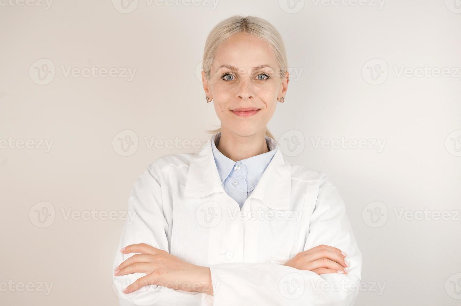 joven médico rubio de pie contra un fondo gris sonriendo a la cámara. foto