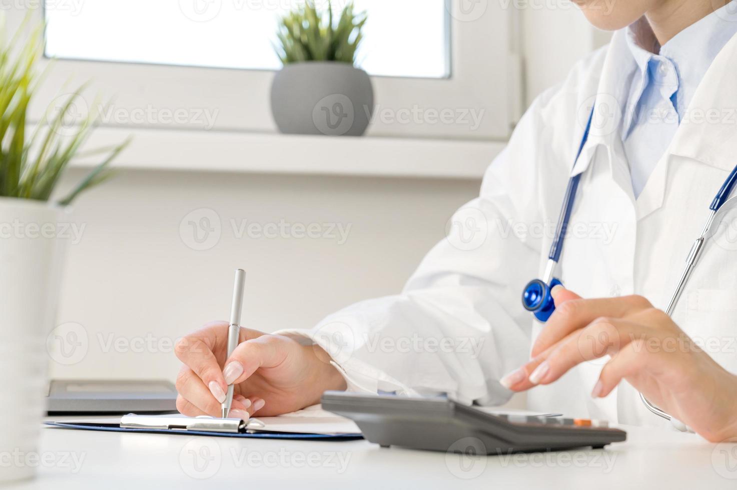 Medical insurance concept . side view on Unrecognizable doctor or nurse with calculator at the table with stethoscope and forms photo