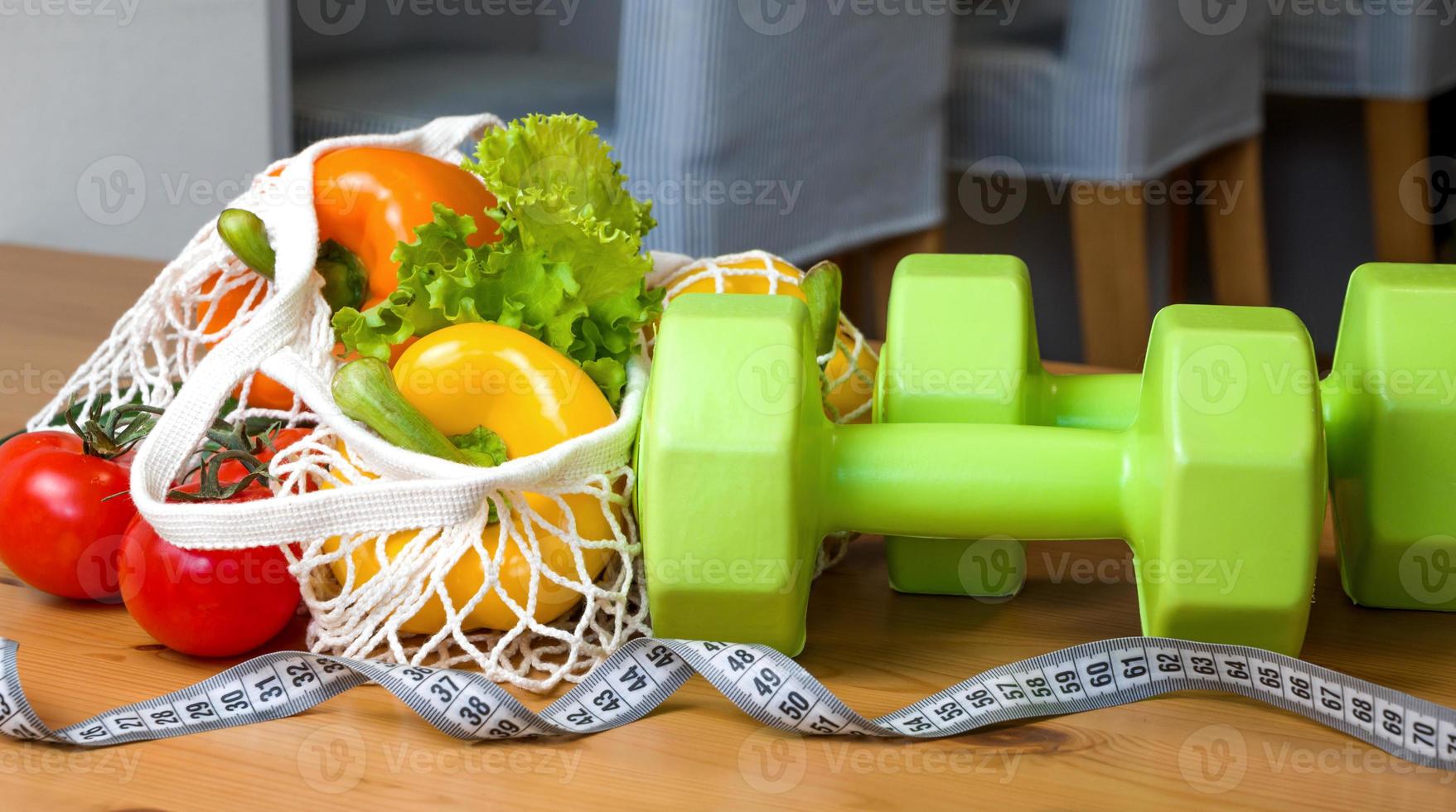 Healthy diet concept. Vegetables in string bag near mesuring tape. Vegetarian,vegan.Sport lifestyle. Dumbbells photo