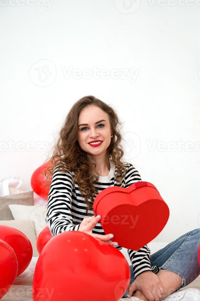 Valentine's day, Women's day. Young funny woman sitting in the bed opening the gift.Vertical shot photo