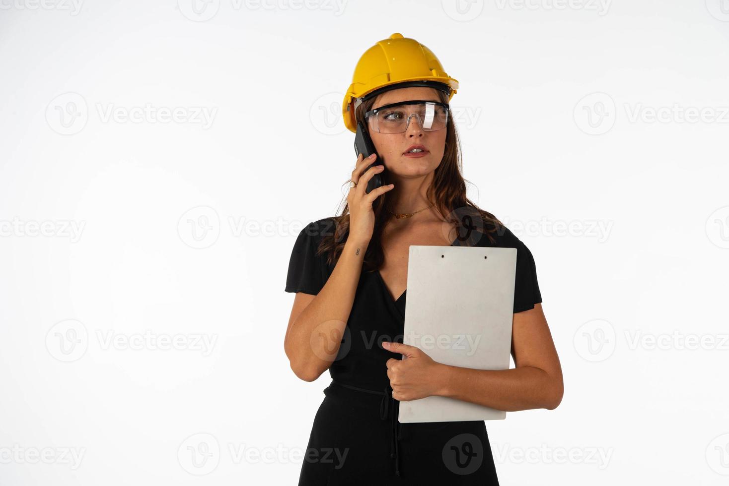 Young beautiful woman engineer holding mobile phone and folder  on isolated white background photo