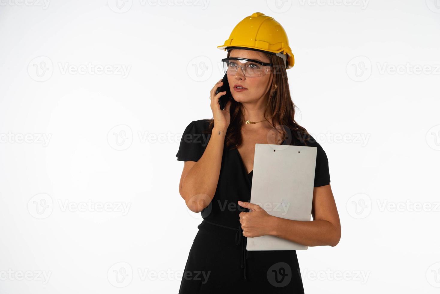 Young beautiful woman engineer holding mobile phone and folder  on isolated white background photo
