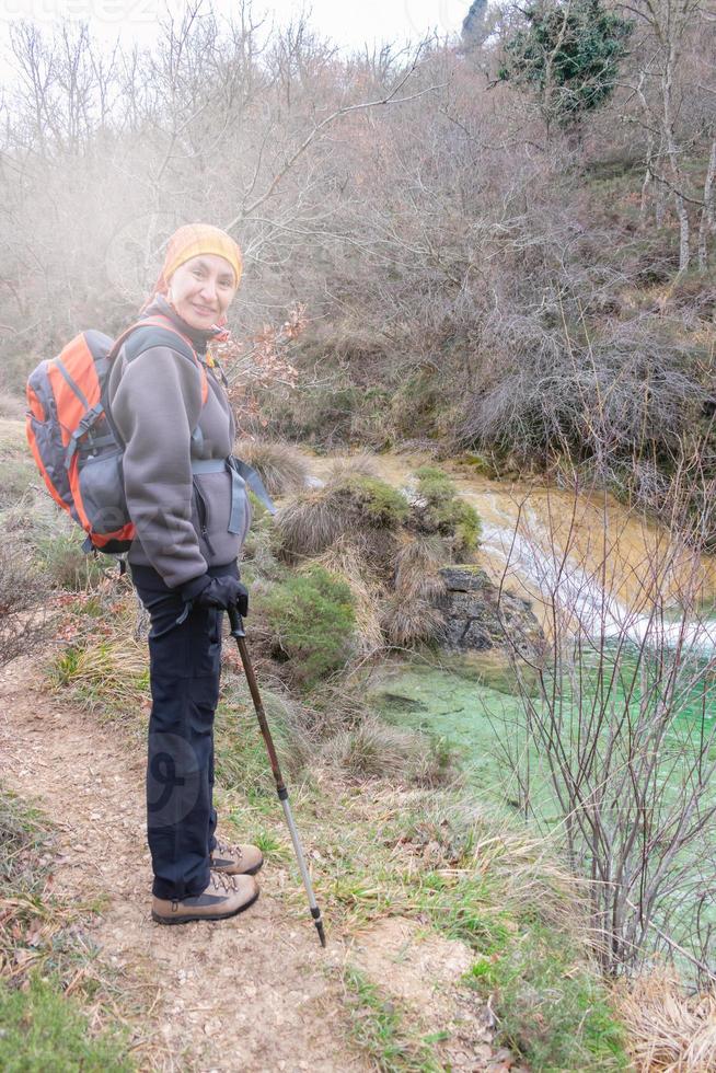 mujer sonriendo mientras camina con mochila al lado del lago de montaña foto