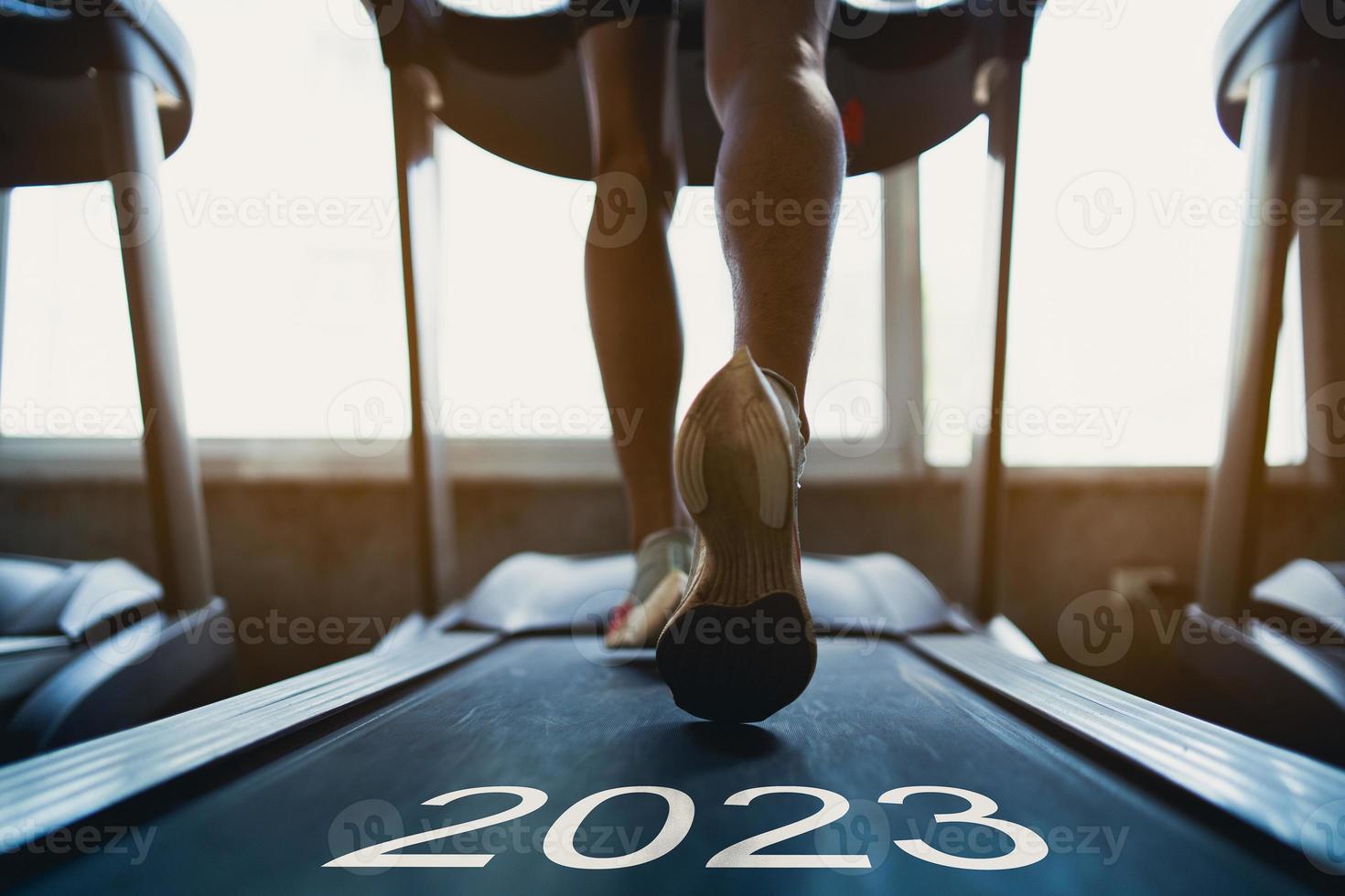 Happy new year 2023,2023 symbolizes the start of the new year. Close up of feet, sportman runner running on treadmill in fitness club. Cardio workout. Healthy lifestyle, guy training in gym. photo