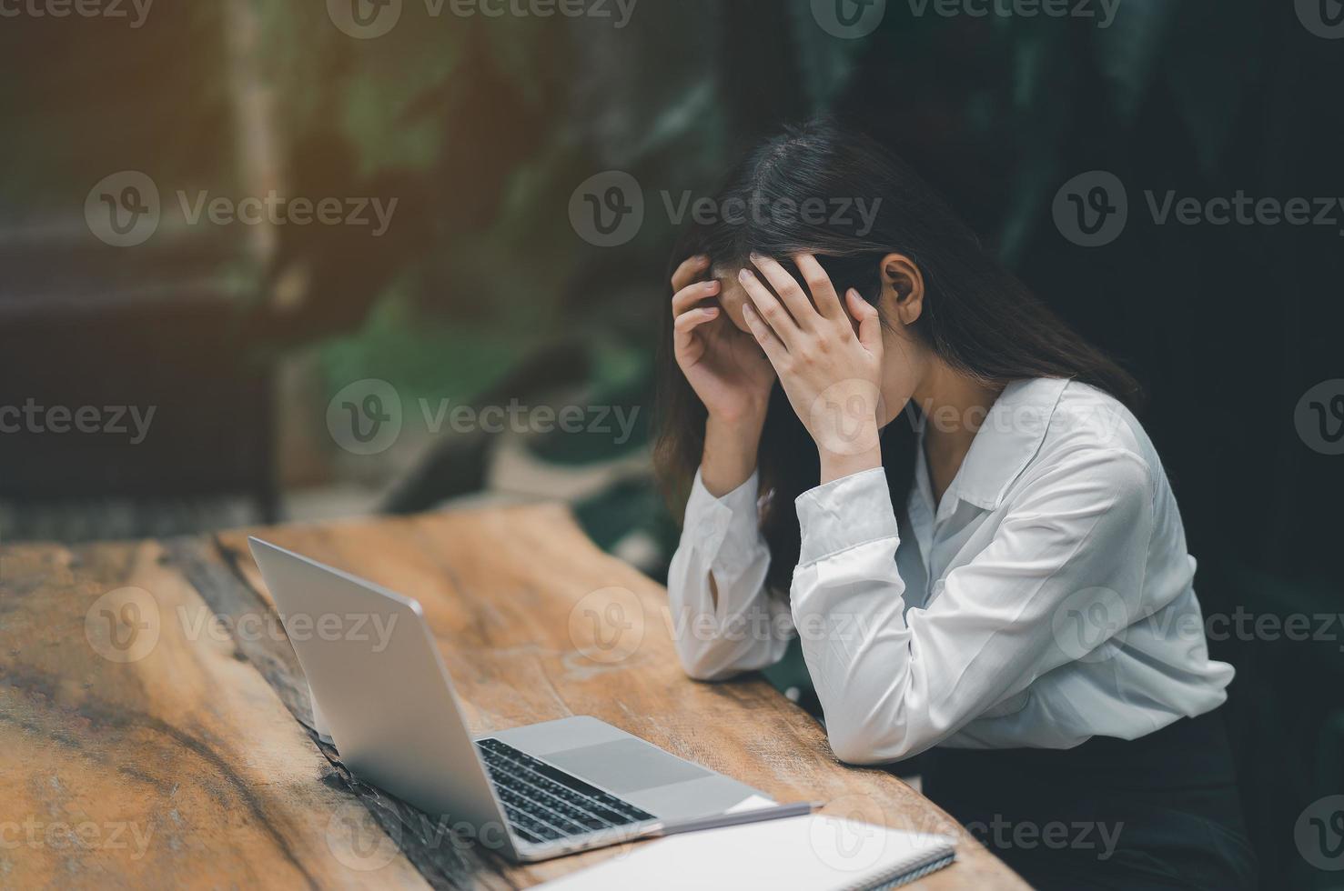 mujer independiente asiática entrega la cabeza con depresión estresante tiempo triste mientras trabaja en una computadora portátil en casa. depresión mujer triste serias trabajando desde casa. trabajando en cualquier lugar concepto. foto