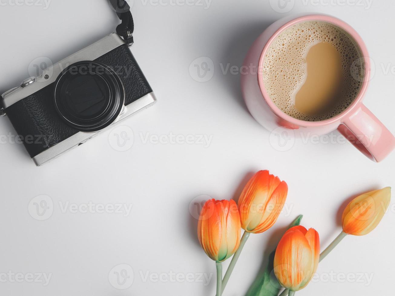 flat lay of camera, pink cup of coffee, and red yellow tuips on white background. photo